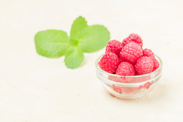 Ripe raspberries with green mint leaves in cup and saucer on pastel yellow background.