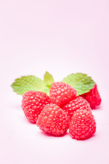 Raw ripe raspberries with fresh green mint leaf isolated on pink pastel background.