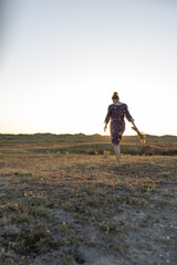 eine frau im hippieblumenkleid in einer heide dünen landschaft zum abendrot