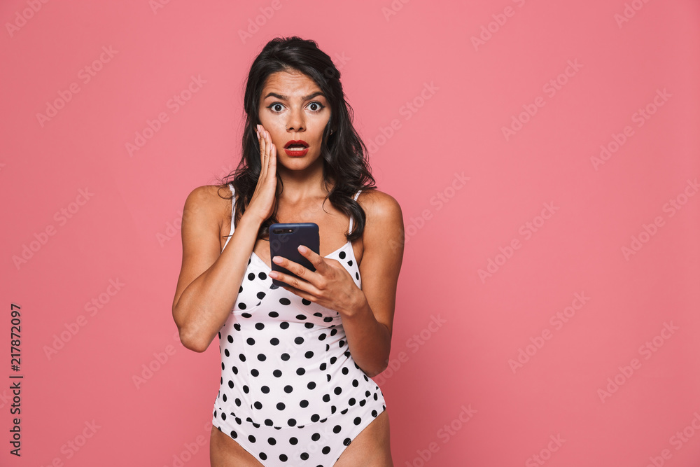 Sticker Shocked woman in swimwear using mobile phone looking camera.