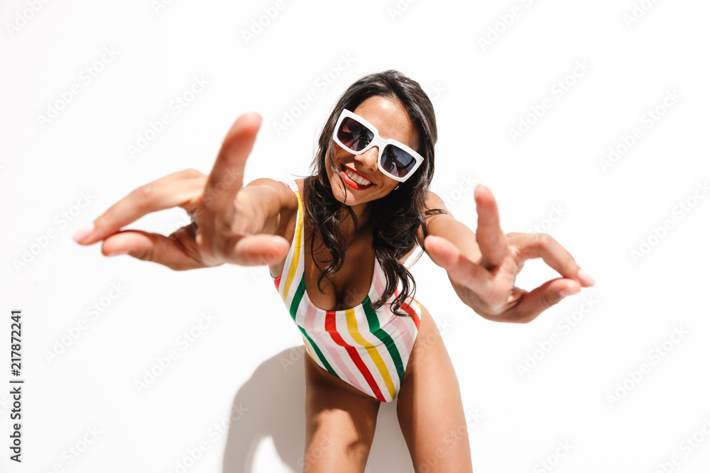 Wall mural woman in swimwear posing isolated over white wall background showing peace gesture.