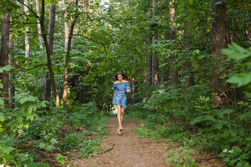 Naklejka na ściany i meble Beautiful young woman in dress runing in the summer forest