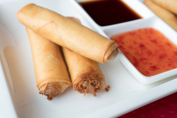 three Chinese pancakes stuffed on a white plate with sweet chili sauce. Shallow depth of field