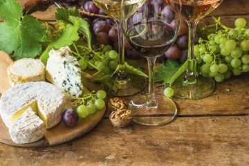 Various of french cheeses, grapes, nuts and glasses of wine of rustic wooden background with copy space