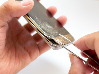 Close-up of technician hand taking off cracked smartphone screen for preparing to repair or replace...