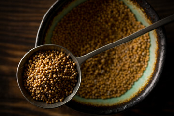 Raw, unprocessed mustard seed kernels in metal scoop on bowl