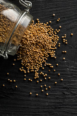 Heap of raw, unprocessed mustard seed kernels in glass jar on black table