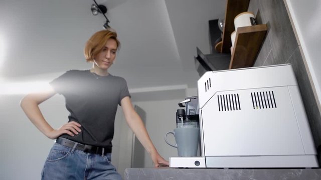 Beautiful young woman with short hair making hot coffee in coffee machine.