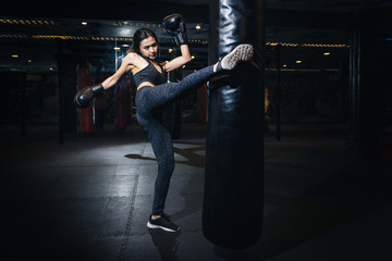 Female boxer hitting a huge punching bag at a boxing studio. Woman boxer training hard. Thai boxer punch kick by punching bag, Black bacground - obrazy, fototapety, plakaty