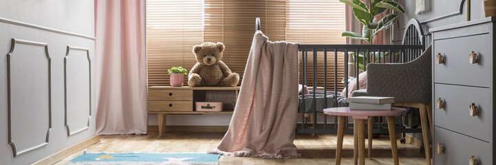 Panorama of a cozy, gray nursery bedroom interior with a classic wooden baby crib and pastel pink...