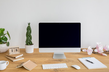 Black desktop computer with mockup on desk with books and plants in work area interior. Real photo