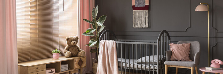 Sweet, pastel pink accessories in a classic, dark nursery bedroom interior with wooden furniture and a gray crib for a child - obrazy, fototapety, plakaty
