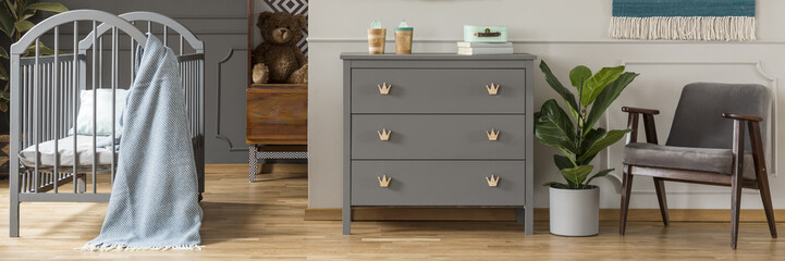 A gray, scandi style dresser with crown-shaped handles in a bright, child bedroom interior with gray, wooden furniture