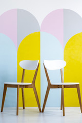 Two chairs set on a patterned wall with yellow accents. Real photo