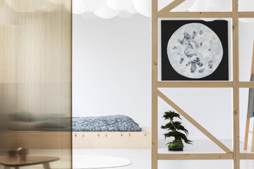 Moon poster on white wall in japanese bedroom interior with sheets on wooden bed. Real photo