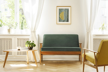 Real photo of a mid-century living room interior with a sofa, coffee table, windows and painting