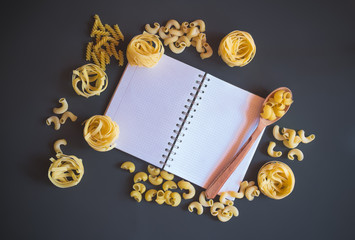 Notepad and raw pasta on dark background.