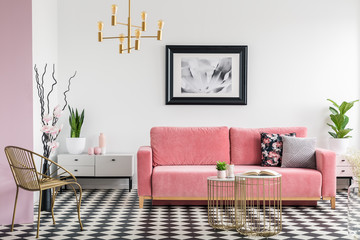 Gold chair and pink sofa in modern living room interior with poster and checkered floor. Real photo