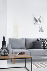 Pillows on grey couch and lanterns on table in minimal living room interior with posters. Real photo