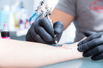 Close-up of the hands of a skilled tattoo artist wearing black gloves while setting a sterile...