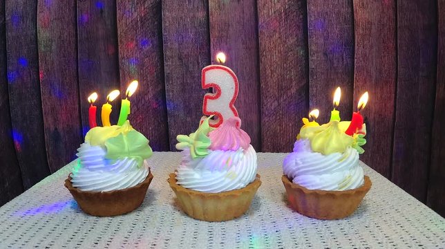 Happy third birthday with number three candle and cakes with wooden background