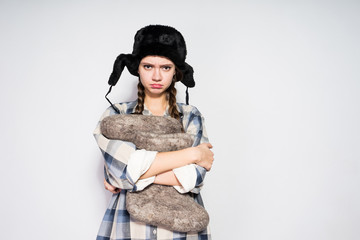 a sad Russian girl in a black fur hat is displeased with something, holding gray winter boots