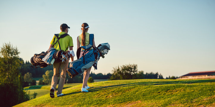 Full length of a happy couple with a healthy lifestyle wearing golf outfits, while carrying stand bags with professional clubs towards the golf course in a sunny day of summer