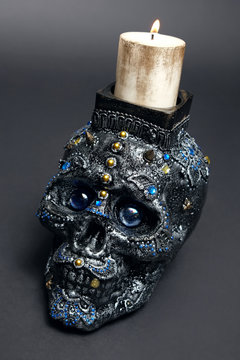 Skull decorated with colorful stones with candle on black background