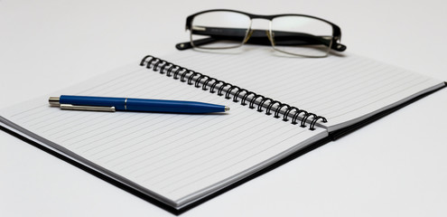 Notebook and glasses and blue pen on table. White background