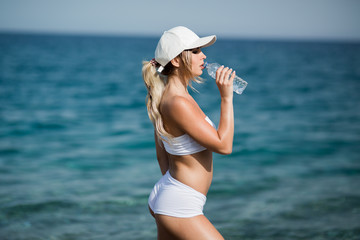 Fototapeta na wymiar Beautiful fitness athlete woman drinking water after work out exercising on the beach outdoor portrait