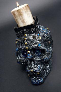 Skull decorated with colorful stones with candle on black background