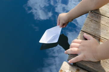 Hands of little boy, releases into the water paper boat with wooden pier.