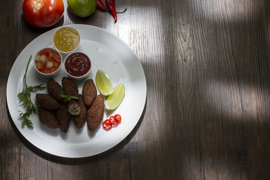Traditional arabic food, kibes served on white plate, accompanied by salad, ketchup, mustard, pepper and lemon on rustic wooden table