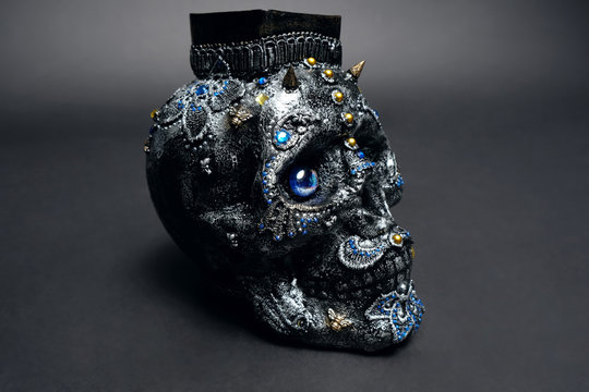 Skull decorated with colorful stones with candle on black background