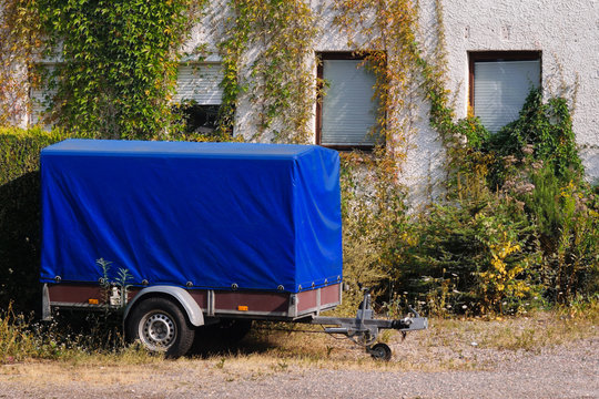 Old blue trailer parked next to an old house with ivy