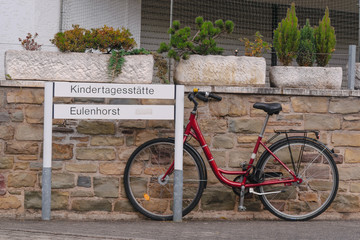 Fototapeta na wymiar Red bike parked on a stone wall next to a street sign