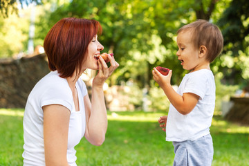 Mother and son eating peach on a picnic in the park. Mom and son sharing one fruit outdoor. Healthy parenting concept