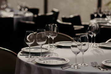 Decorated served table with cutlery and glasses for wedding reception or other festive event. Round table with cutlery, white tableclothes. Empty plates for food