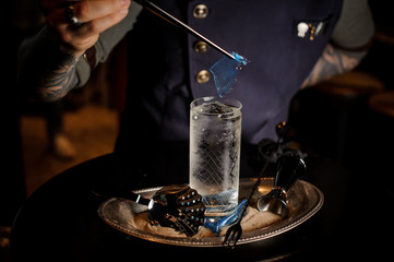Barman with tattoo decorating fresh and sweet summer cocktail with blue piece of caramel on the tray