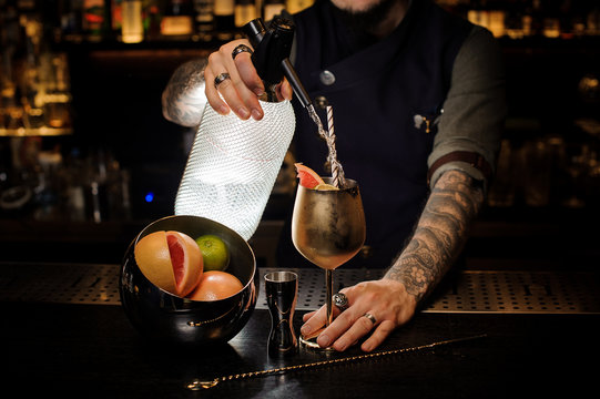 Barman with tattoo pouring cold soda into the copper cocktail glass