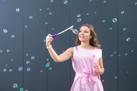 Teenage girl blowing soap bubbles against gray wall