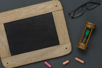 Table top view aerial image of back to school of education season background concept.Flat lay black board with chalk and hourglass on modern rustic wooden plank.Free space for creative design text.