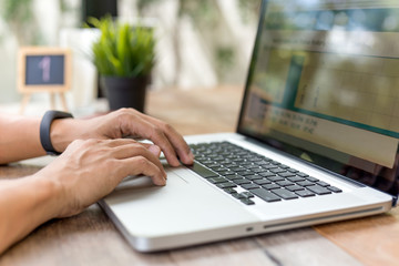 Businessman hands typing on laptop computer on wooden table in cafe.