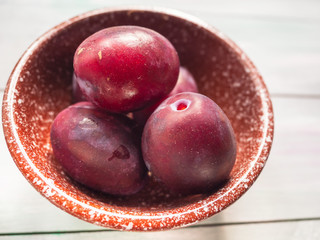 Ripe red plums in a ceramic bowl on a wooden table.
