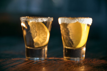 Two glasses of alcohol and lime slices inside, on a dark wooden background