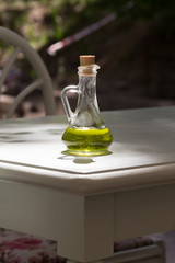 Jug with olive oil on the wooden table. The sun shines on the glass.