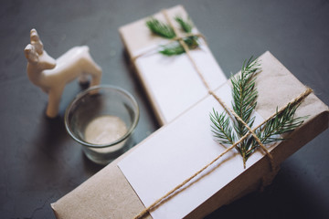 Christmas background with two gift boxes, fir-tree branches, toy deer, candle, decor. Top view with copy space, gray plastered background