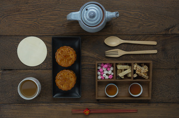 Table top view aerial image of decorations Chinese Moon Festival background concept.Flat lay essential meal set for coffee break of sweet cake & tea with snack on modern rustic brown wooden wallpaper.