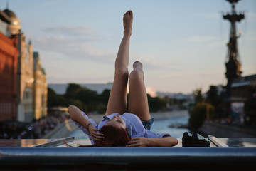 Beautiful Woman with red hair sitting on a roof or bridge, sunset light