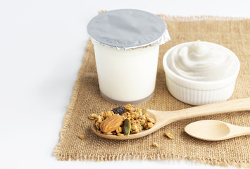 Healthy flavored yogurt in plastic cup and ceramic bowl with cereal and wooden spoon isolated on the white background. With copy space for your text.
